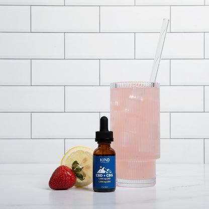 KIND CBD + CBG Tincture  next to a glass of lemonade 