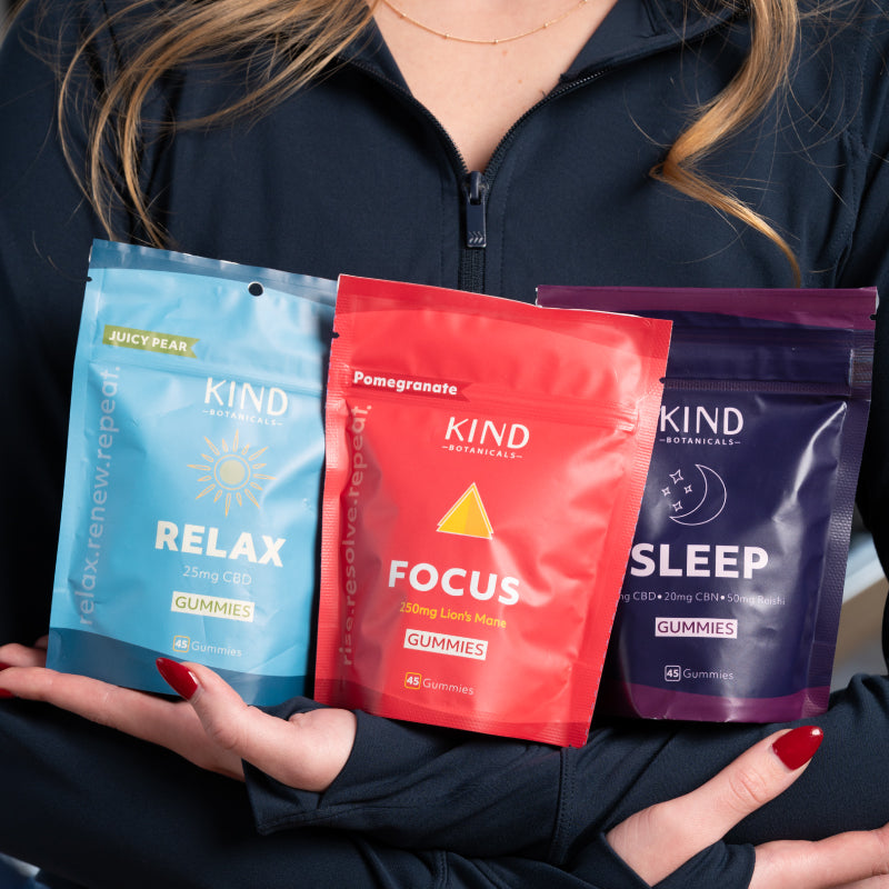Person holding three KIND gummy packages labeled 'Relax', 'Focus', and 'Sleep'.