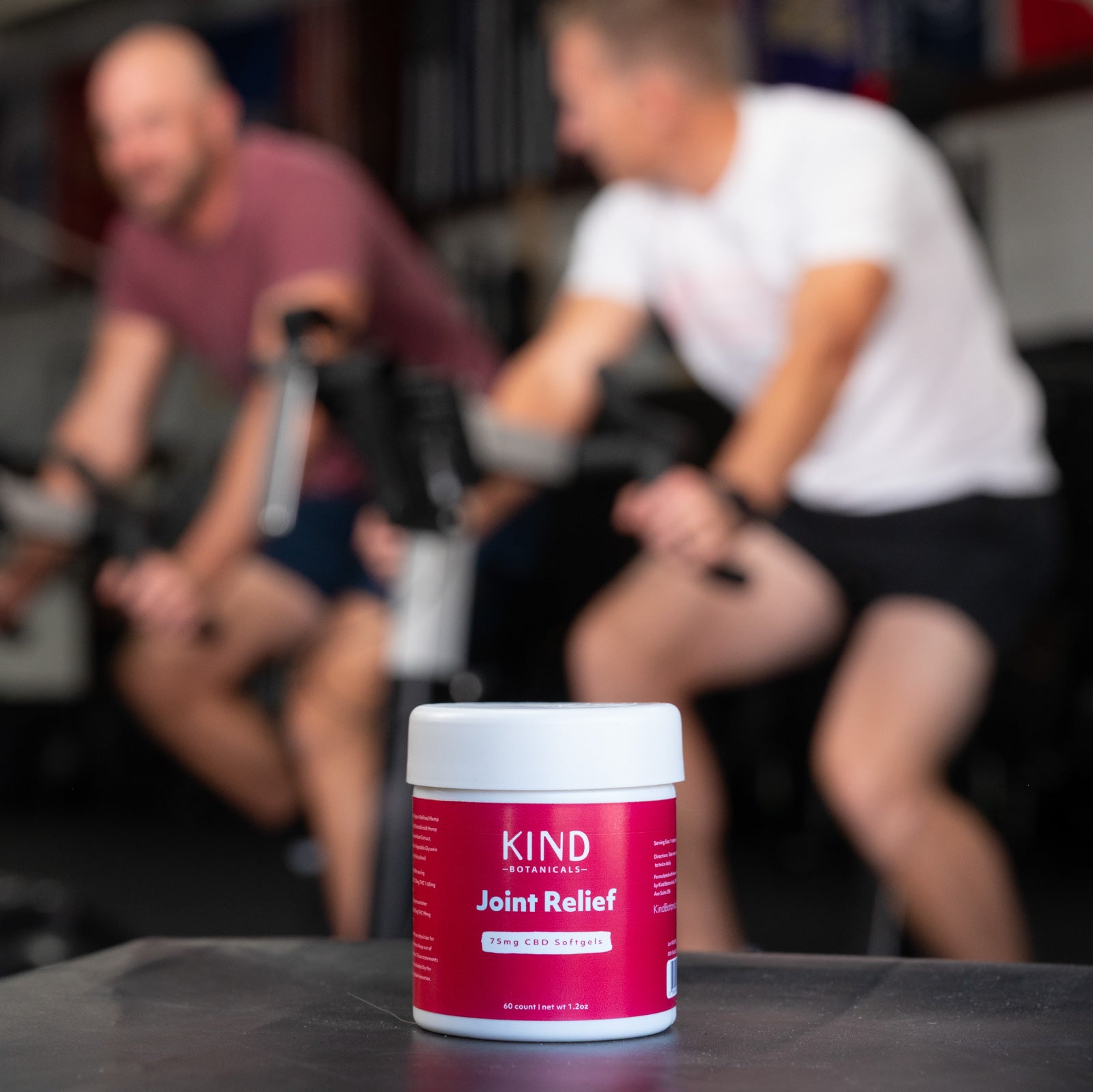 Container of KIND Joint Relief on a table with two people on stationary bikes in the background
