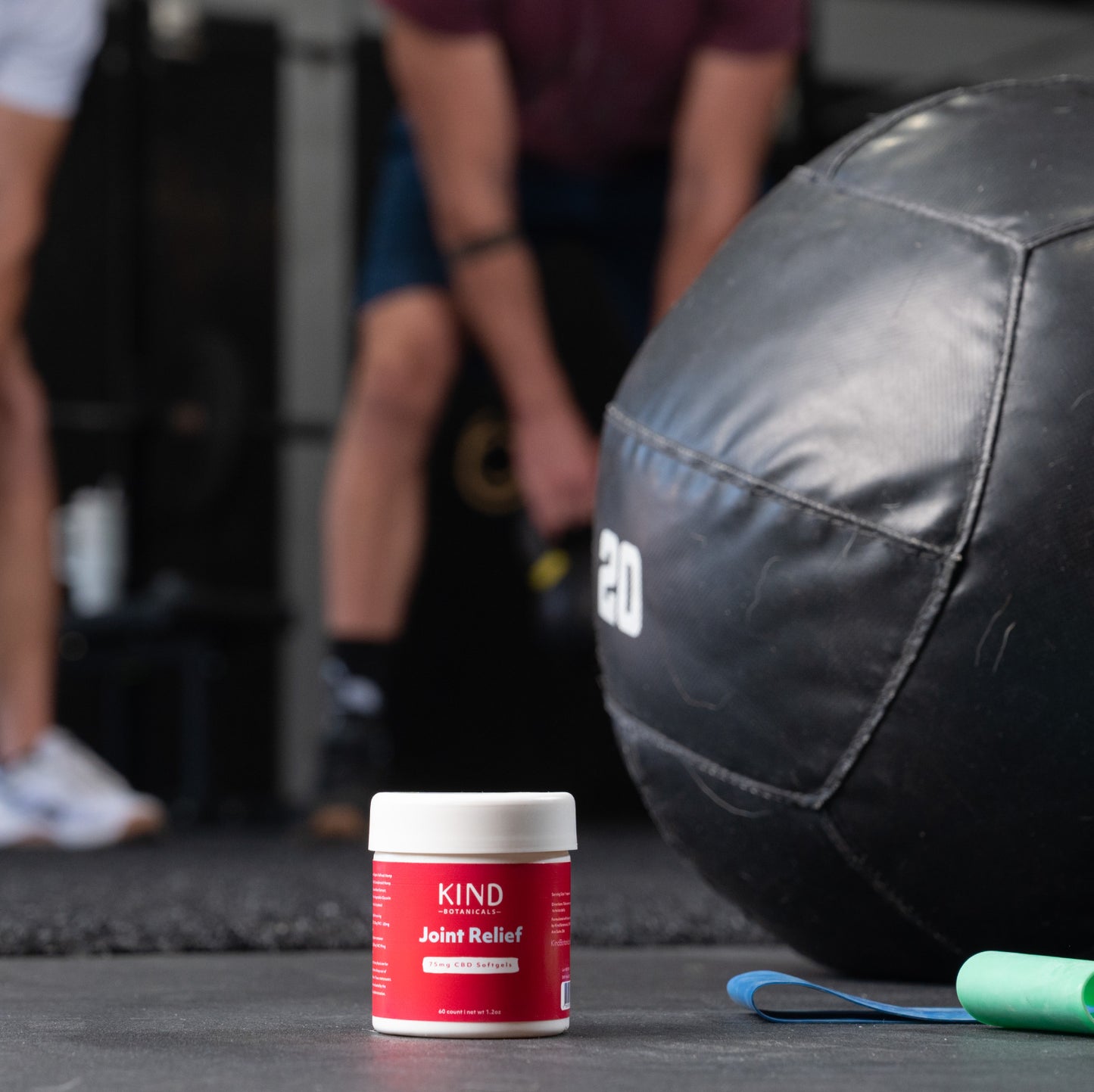 KIND Joint Relief supplement container on a gym floor with exercise equipment in the background