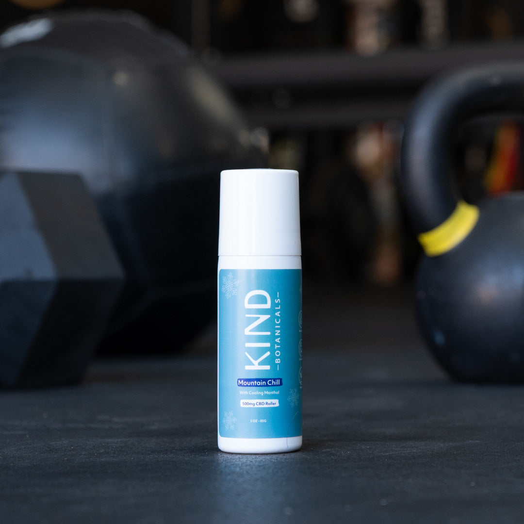 KIND Botanicals mountain chill muscle roll on a gym floor with exercise equipment in the background