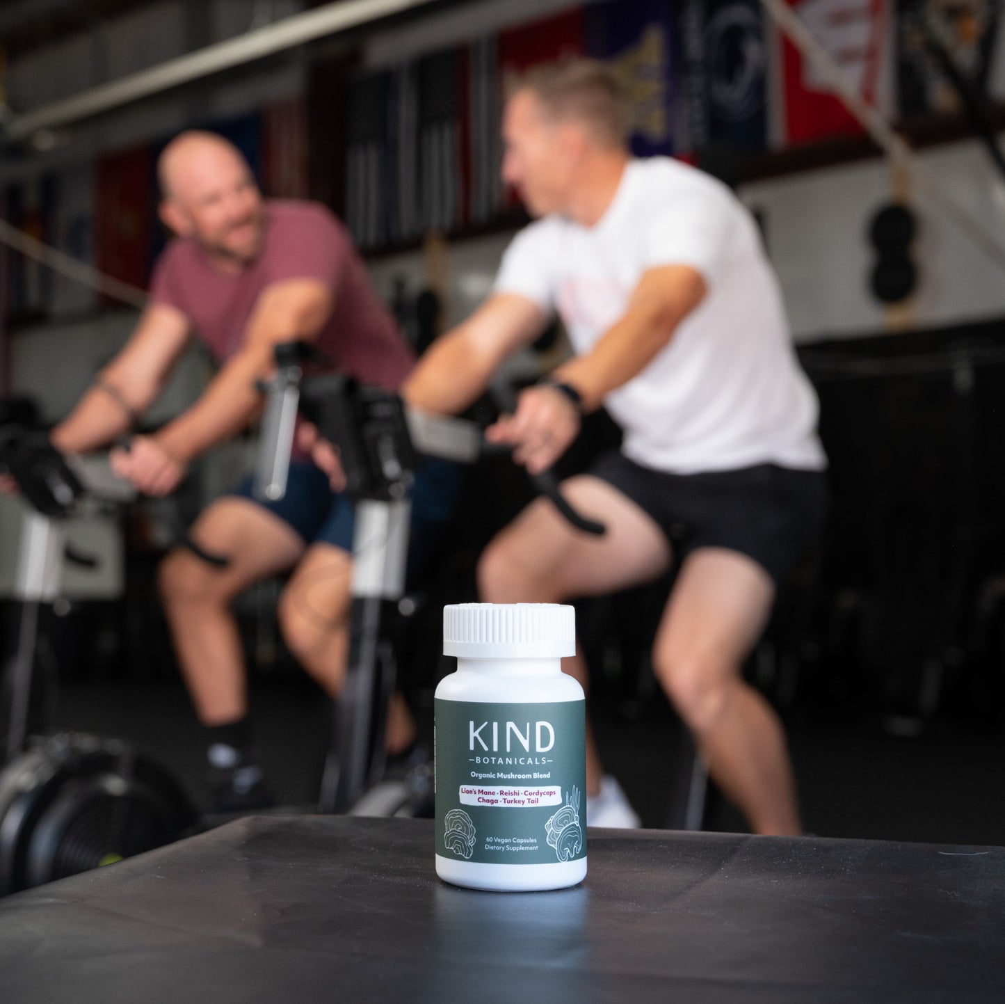 Bottle of Kind Botanicals supplement on a table with two people exercising in the background.