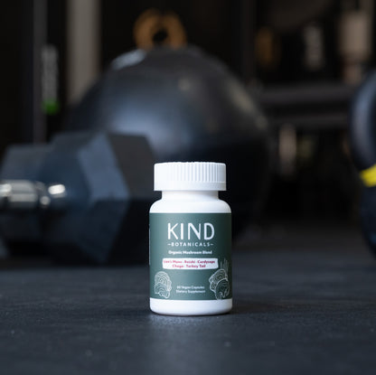 Bottle of Kind Botanicals supplement on a dark surface with gym equipment in the background
