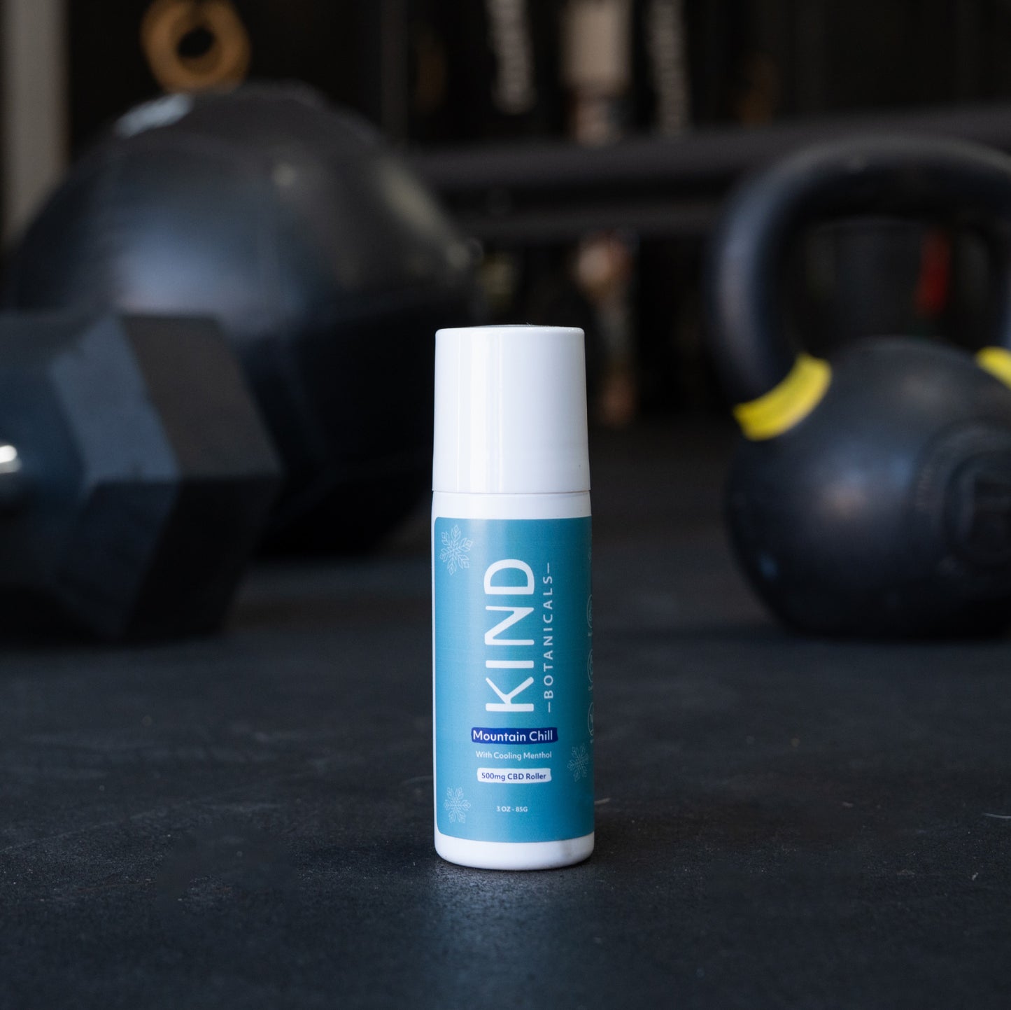 KIND Botanicals product on a dark surface with kettlebells in the background