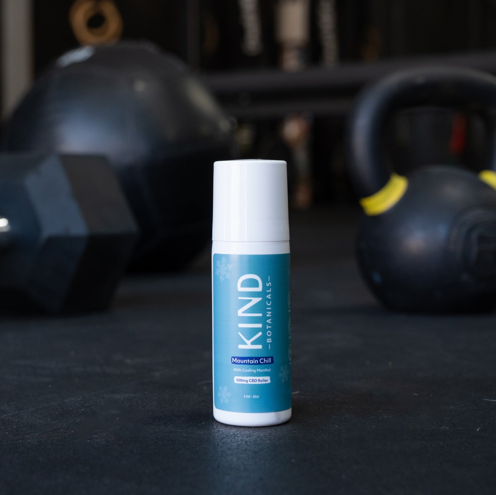 KIND Botanicals product on a dark surface with kettlebells in the background