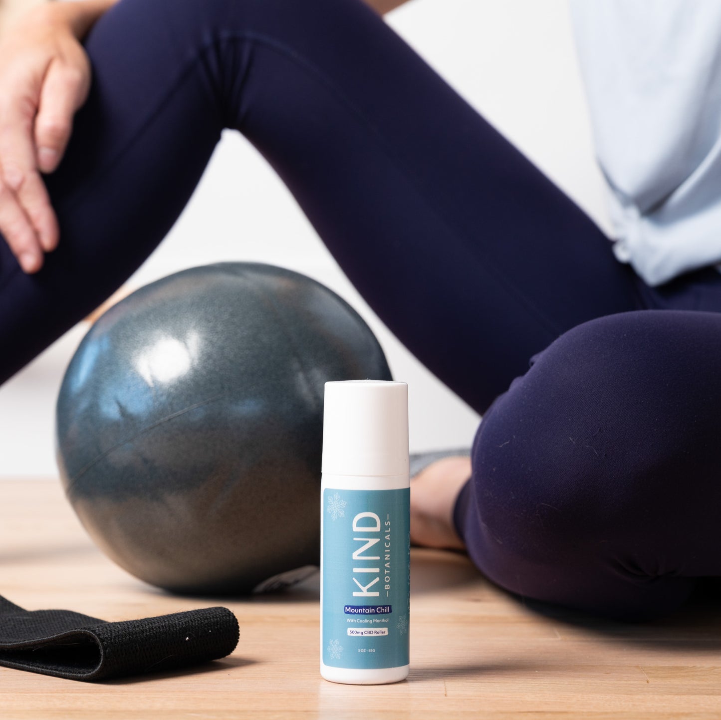 Person sitting on a yoga mat with a fitness ball and a 'KIND' bottle in the foreground.