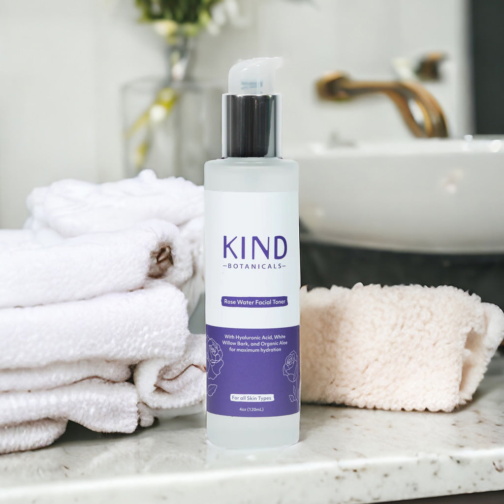 Bottle of KIND Botanicals rose water facial toner on a bathroom counter with towels and a sink in the background.