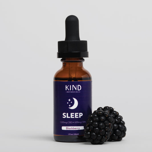 A 1 fl oz amber glass dropper bottle of KIND Botanicals Sleep supplement with a black cap, shown next to two blackberries on a light gray background.