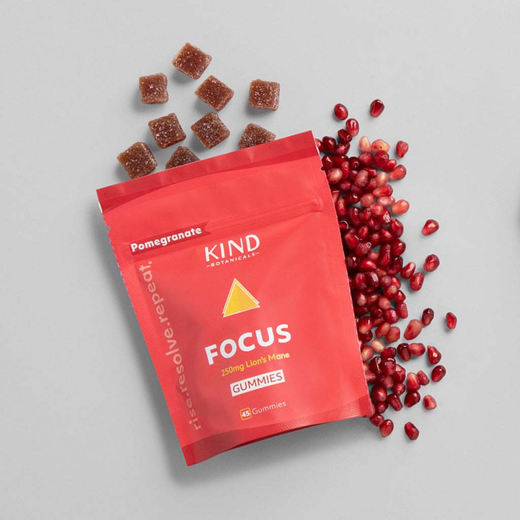 Red KIND Focus Gummies packaging with pomegranate gummies and seeds on a gray background