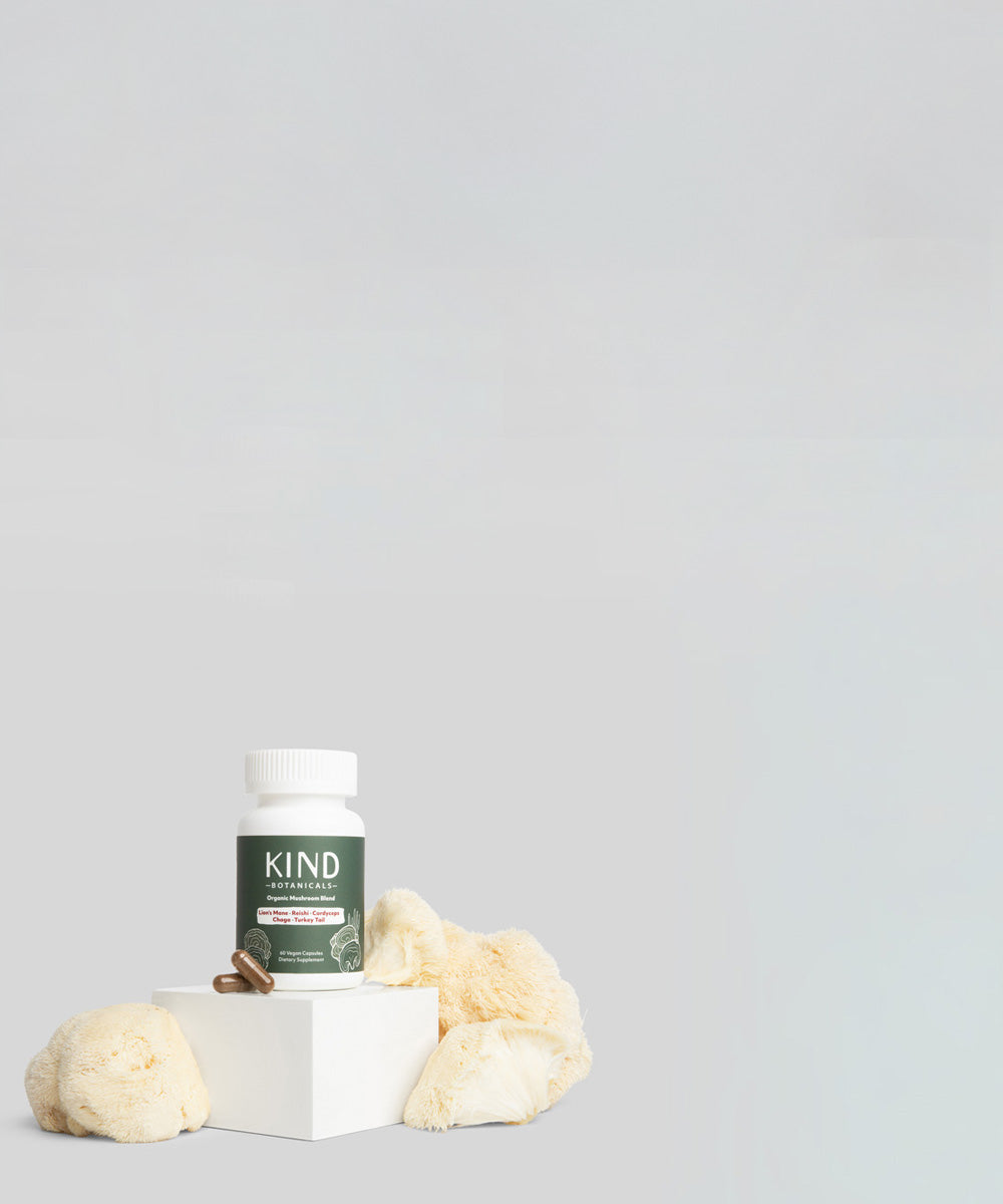 Bottle of KIND Naturals on a white block with loofahs on a light gray background